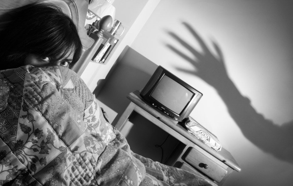 A woman lies in bed while a ghostly vampire shadow hand reaches out for her